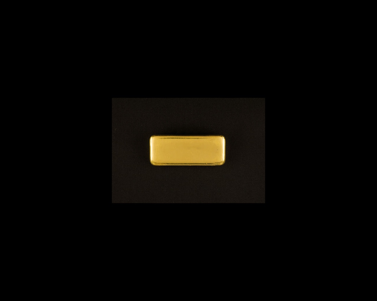 A shiny gold bar with smooth unmarked surfaces and rounded corners, that stands out brightly from a black background