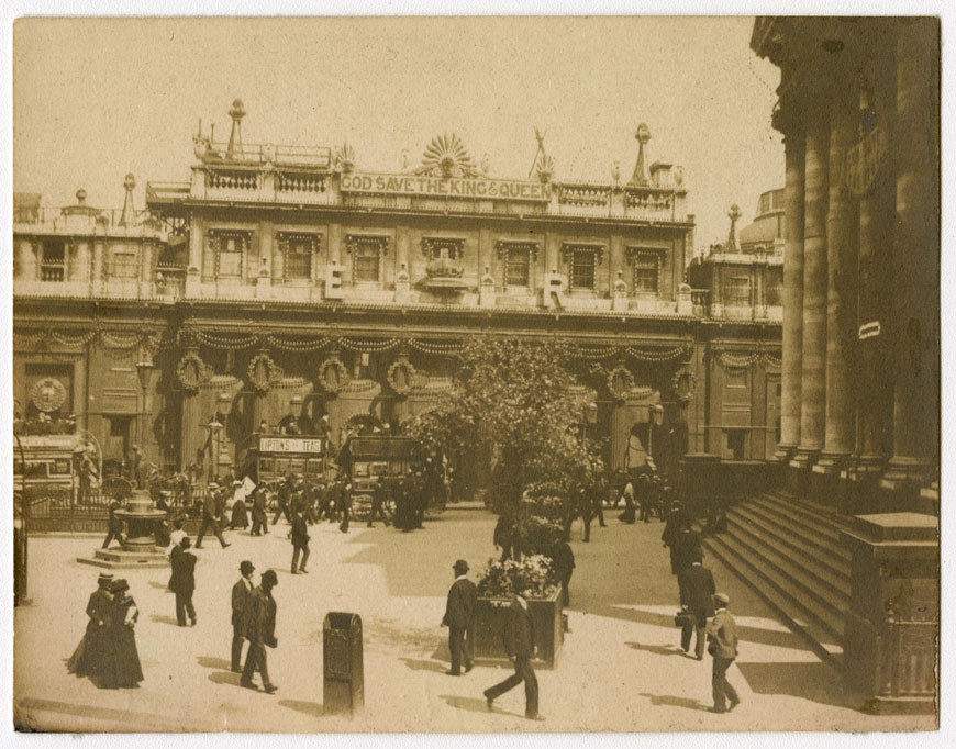 Crowning glories - picture 1 A black and white photograph of the Bank of England at Threadneedle Street in 1902, during the day. The bank is decorated with banners and the initials E R, for the coronation of Edward VII. There are people walking in the outside the Bank and the Royal Exchange, which is shown to the right.